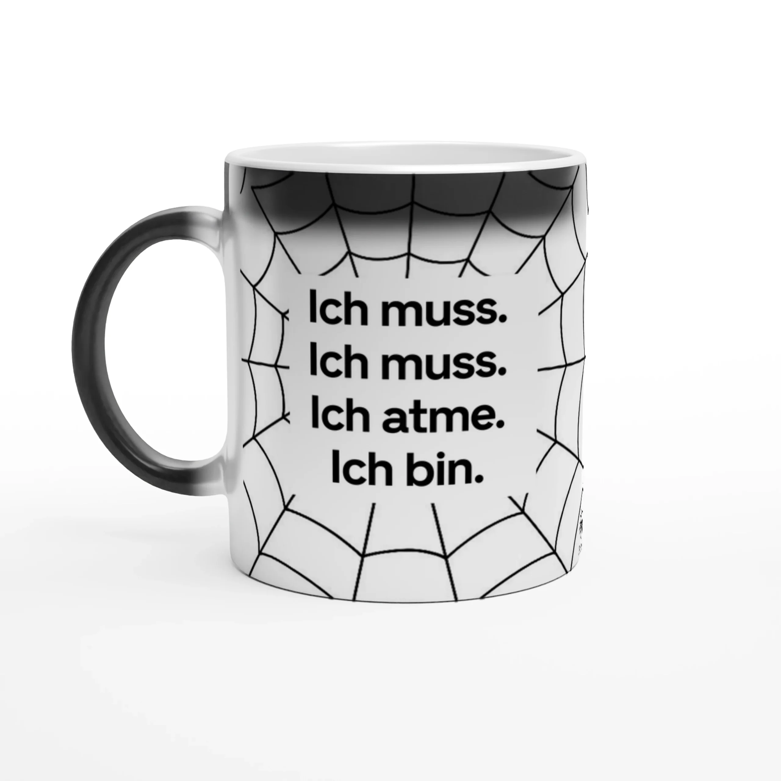 Tasse mit schwarzem Henkel und Spinnennetz-Muster. Auf der Tasse steht: 'Ich muss. Ich muss. Ich atme. Ich bin.'
